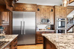 Kitchen featuring built in appliances, light wood-style flooring, light stone countertops, decorative backsplash, and wood finish cabinets