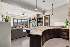 Kitchen with dark wood finish cabinetry, a peninsula, hanging light fixtures, a ceiling fan, and open floor plan