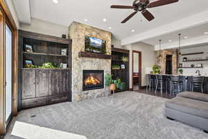 Living area with a stone fireplace, dark carpet, a ceiling fan, beam ceiling, and wet bar