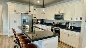 Kitchen featuring stainless steel appliances, an island with sink, a breakfast bar area, and white cabinetry