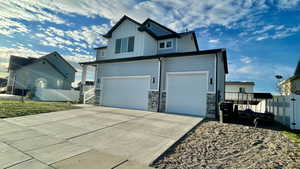 View of side of home featuring concrete driveway, stone siding, a gate, board and batten siding, and a garage