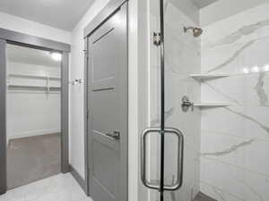 Full bath with a marble finish shower, a walk in closet, and light colored carpet
