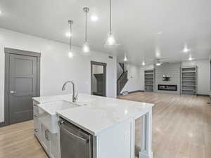 Kitchen with a large fireplace, light wood-type flooring, open floor plan, dishwasher, and a kitchen island with sink