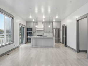Kitchen featuring gray cabinets, light countertops, stainless steel appliances, a kitchen island with sink, and hanging light fixtures