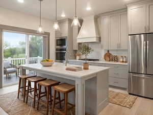 Virtually staged Kitchen featuring stainless steel appliances, light wood-style flooring, a breakfast bar, hanging light fixtures, and a kitchen island with sink
