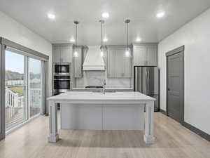 Kitchen with gray cabinetry, pendant lighting, light stone counters, stainless steel appliances, and a center island with sink