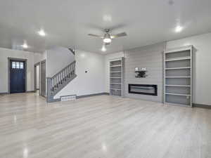 Unfurnished living room with a ceiling fan, a fireplace, and light wood finished floors