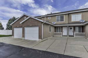 Traditional-style house featuring stucco siding, covered porch, a garage, concrete driveway, and brick siding