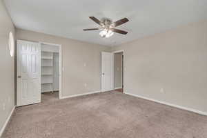 Unfurnished bedroom with a walk in closet, light colored carpet, and ceiling fan