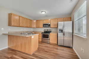 Kitchen with stainless steel appliances, a peninsula, light countertops, light wood finish cabinets, and light wood-style floors