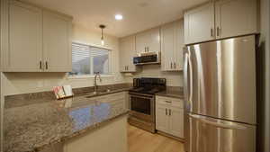 Kitchen with stainless steel appliances, dark stone counters, hanging light fixtures, light wood-style floors, and a peninsula