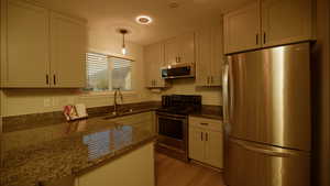 Kitchen with stainless steel appliances, dark stone countertops, hanging light fixtures, and white cabinetry
