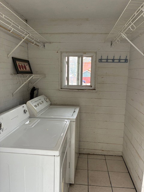 Laundry room featuring wooden walls, washing machine and clothes dryer, light tile patterned flooring, and a barn door