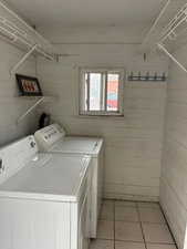 Laundry room featuring wooden walls, washing machine and clothes dryer, light tile patterned flooring, and a barn door