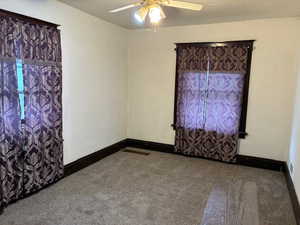 Empty room with dark colored carpet and a ceiling fan