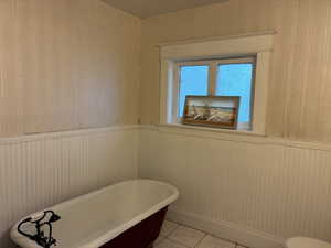 Bathroom featuring wooden walls, a freestanding tub, and light tile patterned floors