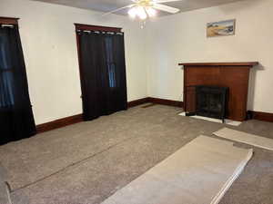 Unfurnished living room with carpet, ceiling fan, and a tile fireplace