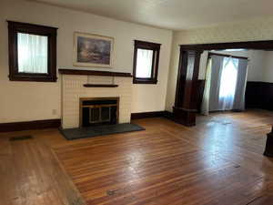 Unfurnished living room featuring dark wood finished floors and a brick fireplace