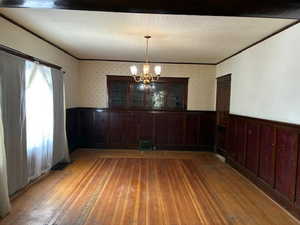Unfurnished dining area featuring wainscoting, ornamental molding, light wood-type flooring, suspended lighting, and wallpapered walls