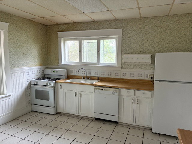 Kitchen with wallpapered walls, white appliances, a drop ceiling, white cabinetry, and light countertops