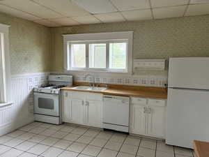 Kitchen with wallpapered walls, white appliances, a drop ceiling, white cabinetry, and light countertops