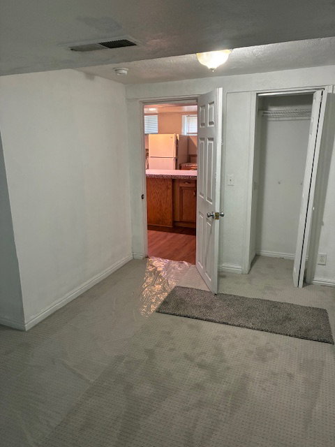 Unfurnished bedroom featuring freestanding refrigerator, light colored carpet, a closet, and ensuite bath