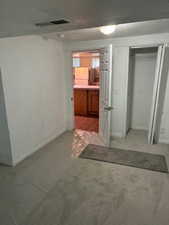 Unfurnished bedroom featuring freestanding refrigerator, light colored carpet, a closet, and ensuite bath