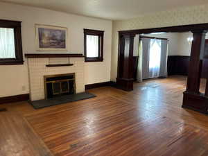 Unfurnished living room featuring hardwood / wood-style floors, ornate columns, and a fireplace