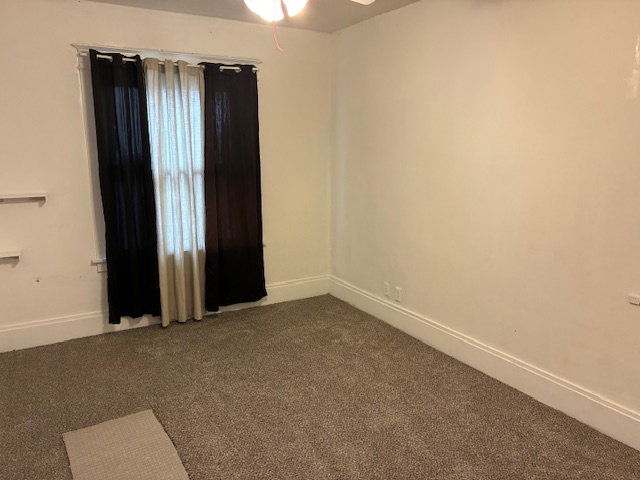 Unfurnished room featuring dark colored carpet and a ceiling fan