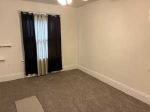 Unfurnished room featuring dark colored carpet and a ceiling fan