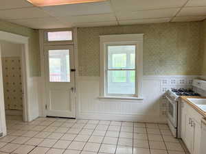 Kitchen with wallpapered walls, white appliances, a paneled ceiling, wainscoting, and light countertops