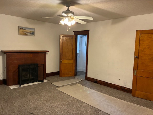 Unfurnished living room featuring carpet, a tile fireplace, ceiling fan, and a textured ceiling
