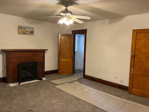 Unfurnished living room featuring carpet, a tile fireplace, ceiling fan, and a textured ceiling