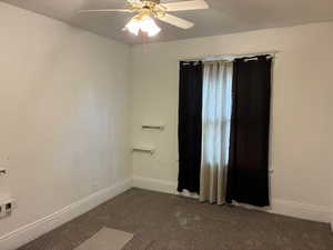 Empty room with ceiling fan and dark carpet