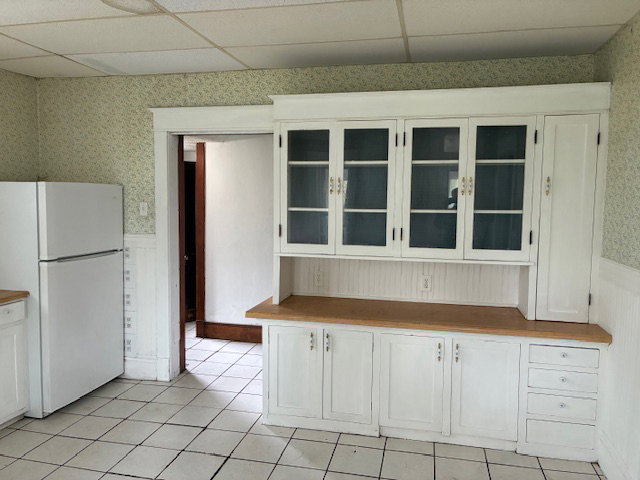 Kitchen with wallpapered walls, wainscoting, white cabinetry, freestanding refrigerator, and butcher block countertops