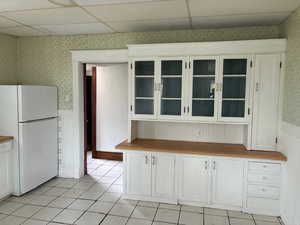 Kitchen with wallpapered walls, wainscoting, white cabinetry, freestanding refrigerator, and butcher block countertops