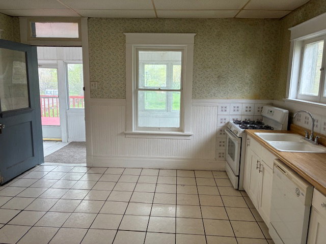 Kitchen featuring wallpapered walls, white appliances, light countertops, a wainscoted wall, and a paneled ceiling