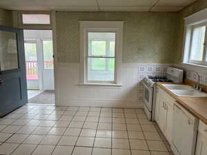 Kitchen featuring wallpapered walls, white appliances, light countertops, a wainscoted wall, and a paneled ceiling