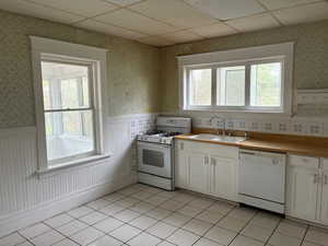 Kitchen featuring wallpapered walls, white appliances, white cabinetry, plenty of natural light, and a drop ceiling
