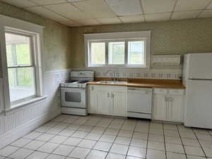 Kitchen featuring white appliances, wallpapered walls, a drop ceiling, white cabinetry, and light tile patterned flooring