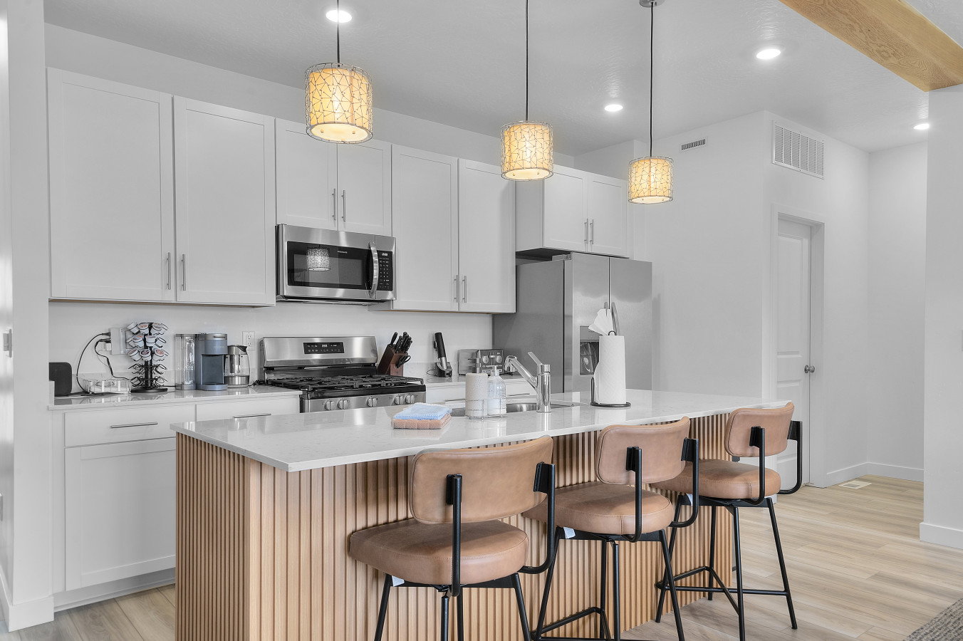 Kitchen accented with stainless steel appliances, upgraded lighting, quartz countertops and kitchen bar designed with fluted paneling.