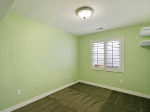 Unfurnished room featuring dark colored carpet and a textured ceiling