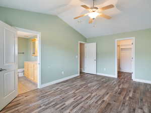 Unfurnished bedroom featuring a walk in closet, vaulted ceiling, ceiling fan, dark wood-style flooring, and ensuite bath