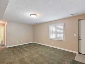 Unfurnished room featuring a textured ceiling and dark carpet