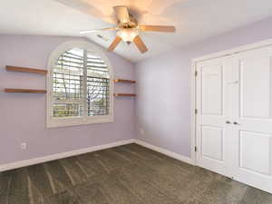 Unfurnished bedroom with dark colored carpet, a closet, vaulted ceiling, and a ceiling fan