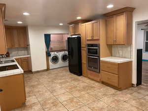 Kitchen with tasteful backsplash, tile counters, washing machine and clothes dryer, black refrigerator with ice dispenser, and recessed lighting