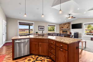 Kitchen with stainless steel dishwasher, an island with sink, a stone fireplace, light stone counters, and open floor plan