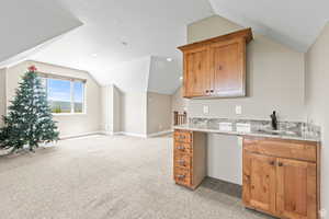 Kitchen with light stone counters, light colored carpet, a textured ceiling, wood finish cabinetry, and open floor plan