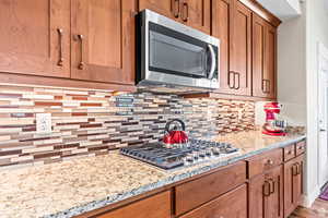 Kitchen featuring stainless steel appliances, light stone countertops, wood finish cabinetry, and decorative backsplash