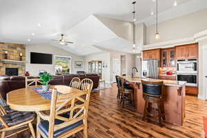 Dining room with dark wood-style floors, a stone fireplace, ceiling fan, and a high ceiling
